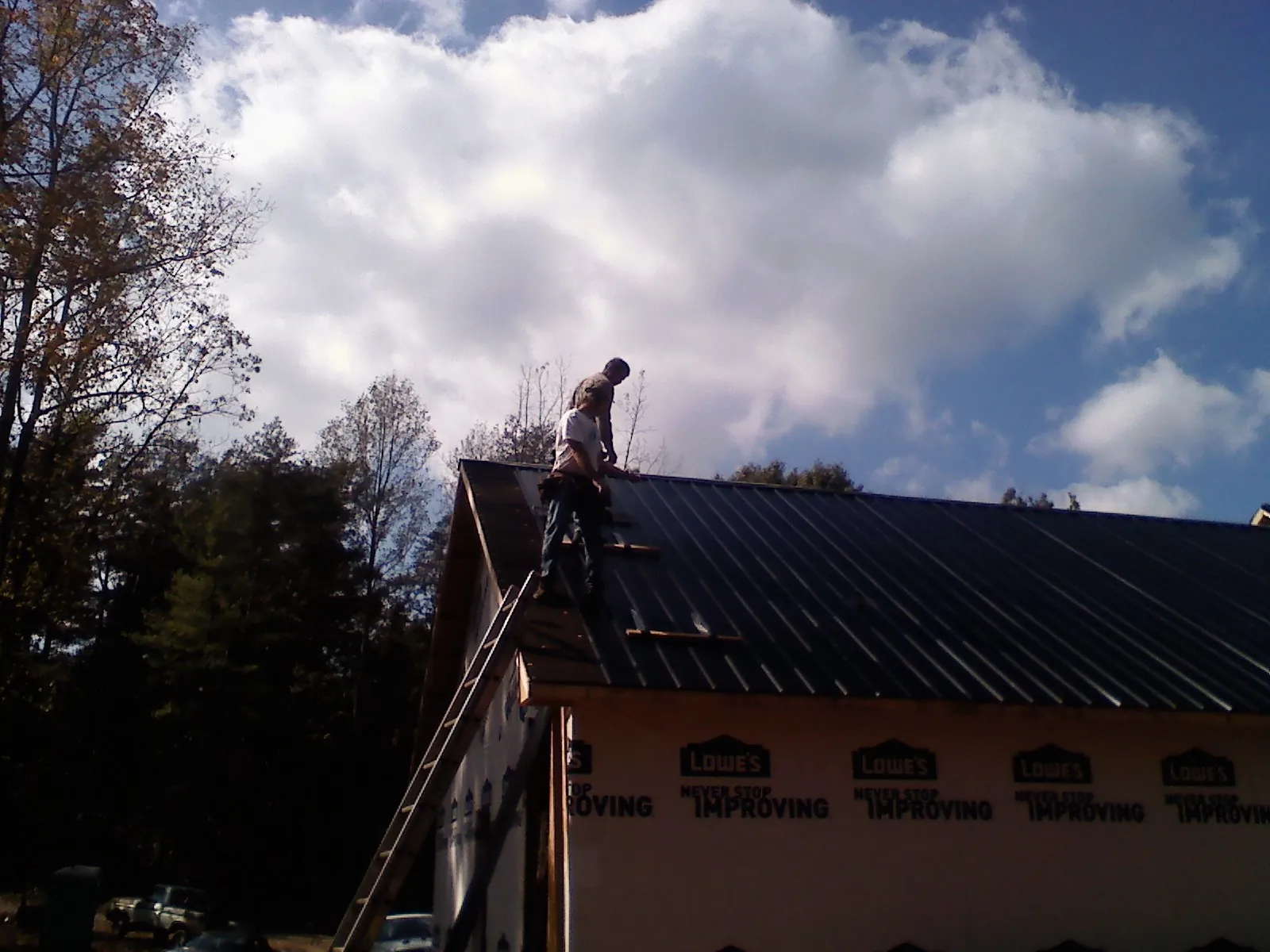 Roofer fastening dark metal panels high against a cloudy sky, from a Roof Inspection job in Neah Bay