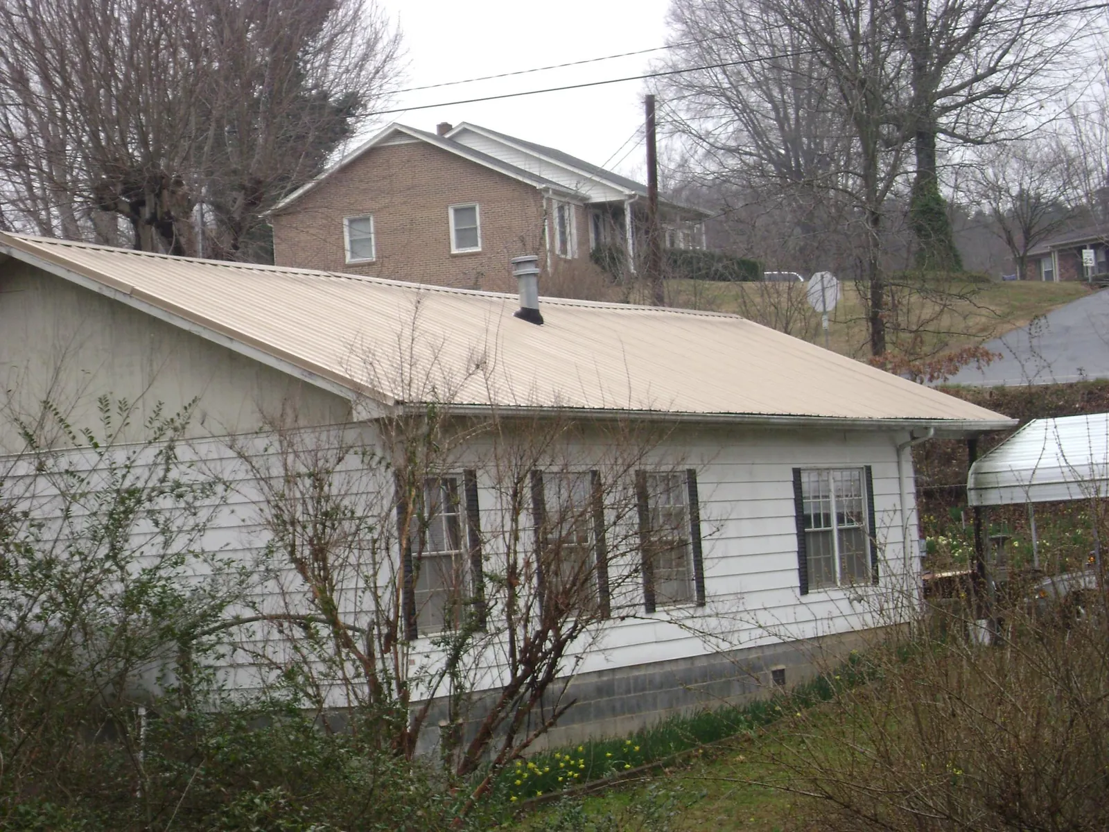Tan metal roof on a white sided house set into a hillside — Commercial Roofing by Roofing Brothers in Neah Bay